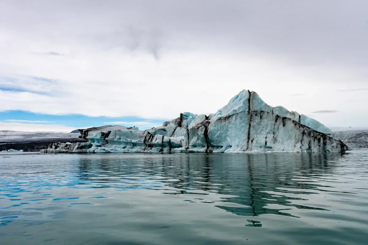 A striped iceberg of white and blue ice reflected in still water on a Jökulsárlón glacier lagoon boat tour